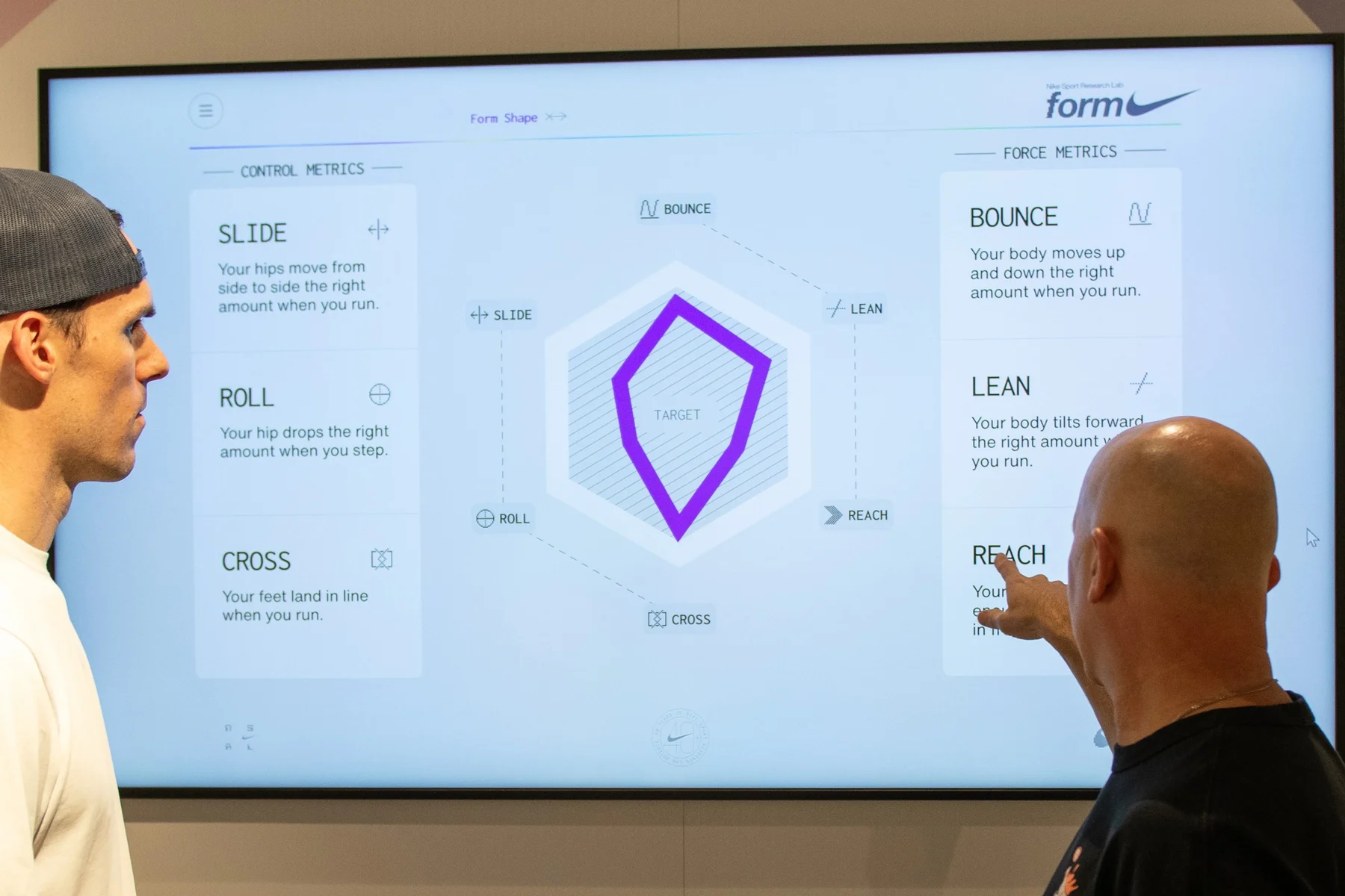 Two runners reviewing their results on a large in-store display showing control and force metrics